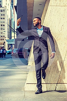 Young African American Businessman with beard, stretching arm, taking selfie on cell phone outside office in New York City