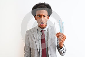 Young african american businessman holding boarding pass over isolated white background scared in shock with a surprise face,