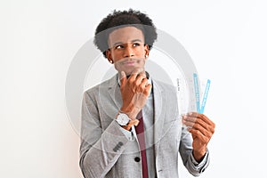 Young african american businessman holding boarding pass over isolated white background serious face thinking about question, very