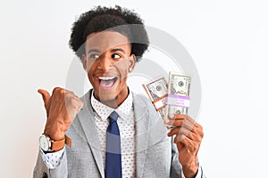 Young african american businessman holding dollars standing over isolated white background pointing and showing with thumb up to