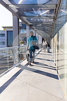 Young african american businessman with luggage walking ahead of businesswoman at airport corridor