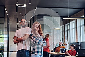 A young African American businessman and a modern businesswoman with orange hair stand side by side, arms crossed