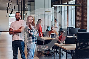 A young African American businessman and a modern businesswoman with orange hair stand side by side, arms crossed