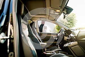 Young african american businessman opening his new car door. Side view, sunny day