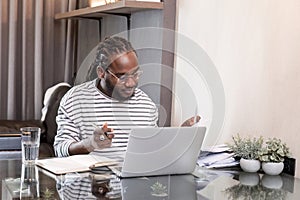 Young African American businessman spends his free time working from home on his laptop.