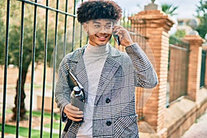 Young african american businessman talking on the smartphone holding bottle of water at the city