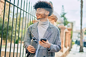 Young african american businessman using smartphone holding bottle of water at the city