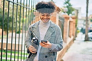 Young african american businessman using smartphone holding bottle of water at the city