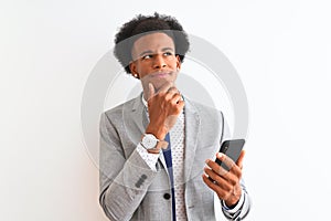 Young african american businessman using smartphone over isolated white background serious face thinking about question, very