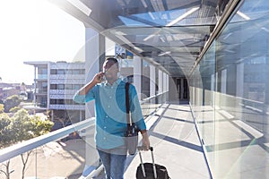 Young african american businessman walking with luggage while talking on smartphone at airport