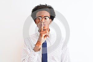 Young african american businessman wearing tie and glasses over isolated white background asking to be quiet with finger on lips