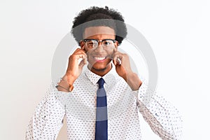 Young african american businessman wearing tie and glasses over isolated white background covering ears with fingers with annoyed