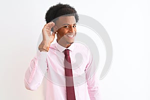 Young african american businessman wearing tie standing over isolated white background smiling with hand over ear listening an