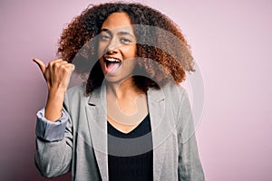 Young african american businesswoman with afro hair wearing elegant jacket smiling with happy face looking and pointing to the