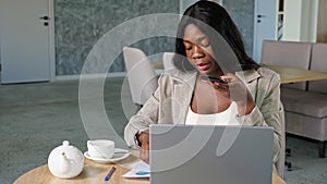 Young African-American businesswoman with documents in grey jacket records audio message on modern cellphone sitting at