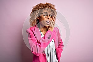 Young african american businesswoman wearing glasses standing over pink background hand on mouth telling secret rumor, whispering