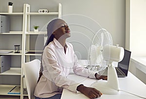 Young african american woman working at office using electric fan during heatwave in office. photo