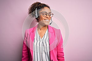 Young african american call center agent girl wearing glasses working using headset looking away to side with smile on face,