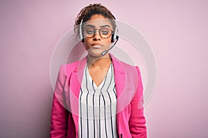 Young african american call center agent girl wearing glasses working using headset with serious expression on face