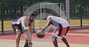 Young african american and caucasian basketball players playing at outdoor court, practicing attack and defence