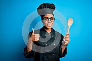 Young african american chef girl wearing cooker uniform and hat holding wooden spoon tool happy with big smile doing ok sign,
