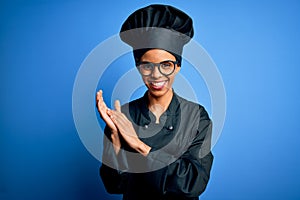 Young african american chef woman wearing cooker uniform and hat over blue background clapping and applauding happy and joyful,