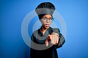 Young african american chef woman wearing cooker uniform and hat over blue background pointing displeased and frustrated to the