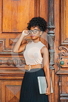 Young African American College Student with afro hairstyle, eye glasses, wearing sleeveless light color top, black skirt, belt,