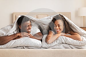 Young African American Couple Lying Under Blanket In Bedroom