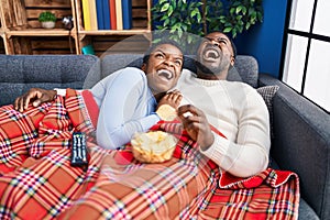 Young african american couple sitting on the sofa watching tv angry and mad screaming frustrated and furious, shouting with anger