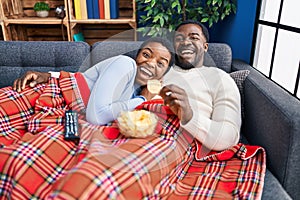 Young african american couple sitting on the sofa watching tv celebrating crazy and amazed for success with open eyes screaming