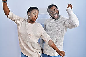 Young african american couple standing over blue background together dancing happy and cheerful, smiling moving casual and