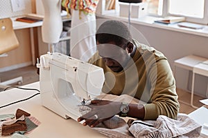 Young African American couturier using electric sewing machine