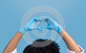 Young african american curly woman doctor in white coat and protective gloves make heart sign with hands