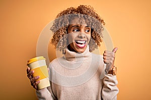 Young african american curly woman drinking cup of takeaway coffee over yellow background pointing and showing with thumb up to