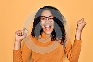 Young african american curly woman wearing glasses eating delicious french dessert macaron screaming proud and celebrating victory