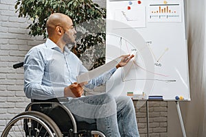 Young african american disabled man in a wheelchair makes presentation at office on whiteboard