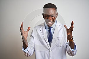 Young african american doctor man wearing coat standing over isolated white background celebrating mad and crazy for success with