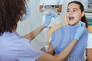 Young african american doctor in uniform, protective mask and gloves treats teeth of hispanic girl