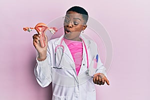 Young african american doctor woman holding anatomical model of female genital organ scared and amazed with open mouth for