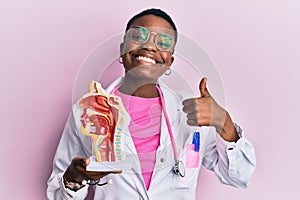Young african american doctor woman holding anatomical model of respiratory system smiling happy and positive, thumb up doing