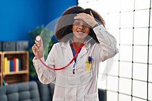 Young african american doctor woman wearing doctor uniform and stethoscope stressed and frustrated with hand on head, surprised