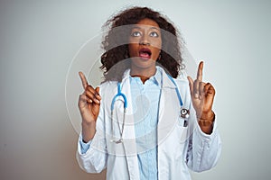 Young african american doctor woman wearing stethoscope over isolated white background amazed and surprised looking up and