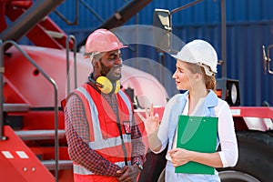 A young African-American engineer and Caucasian woman manager monitor and supervise the loading of containers at a commercial