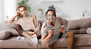 Young african american family couple disagree on tv channel choice while sitting on sofa at home