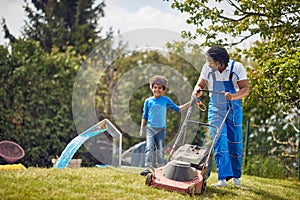 Young african american father mowing grass outdoors with his young son. Working together in the backyard