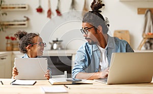 Young african american father works remotely on laptop while his little son using digital tablet