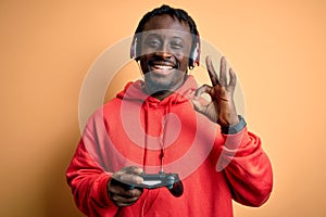Young african american gamer man playing video game using joystick and headphones doing ok sign with fingers, excellent symbol