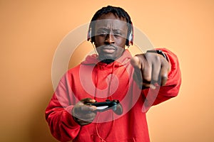 Young african american gamer man playing video game using joystick and headphones pointing with finger to the camera and to you,