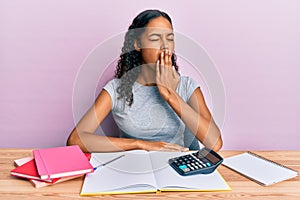 Young african american girl accountant working at the office bored yawning tired covering mouth with hand